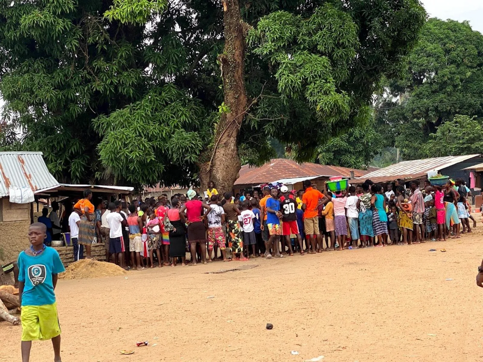 A large community gathering under a mango tree in a Gbema partner village in Sierra Leone
