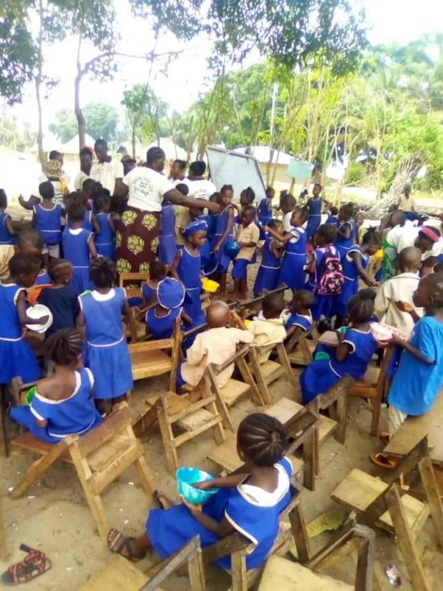 Schoolchildren in blue uniforms gathered for an outdoor class on wooden chairs