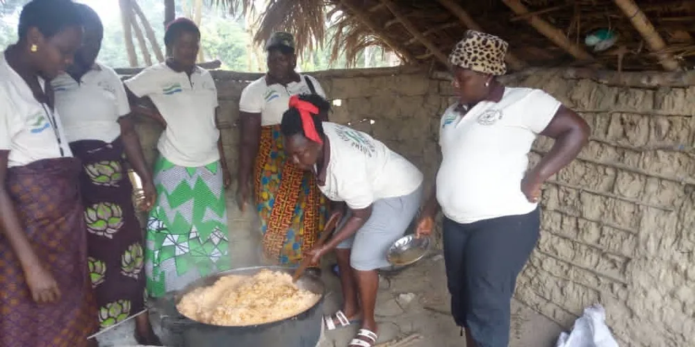 Community women in Gbema shirts cooking a large pot of food for a school meal